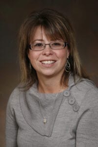 A woman with glasses and a gray sweater.
