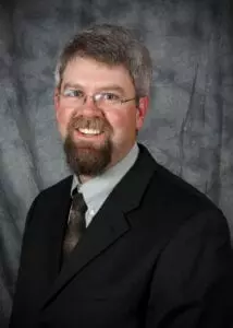 A man with a beard and glasses in a suit.