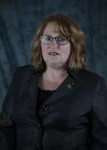 A woman with glasses and red hair wearing a black jacket.