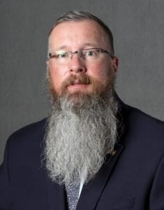 A man with long beard and glasses in a suit.