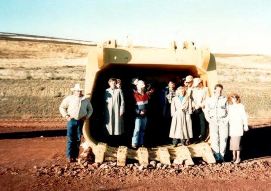 A group of people standing in front of an excavator.