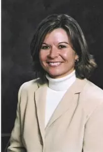 A woman in a tan jacket and white shirt.
