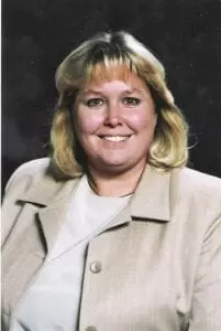 A woman in a tan jacket smiling for the camera.