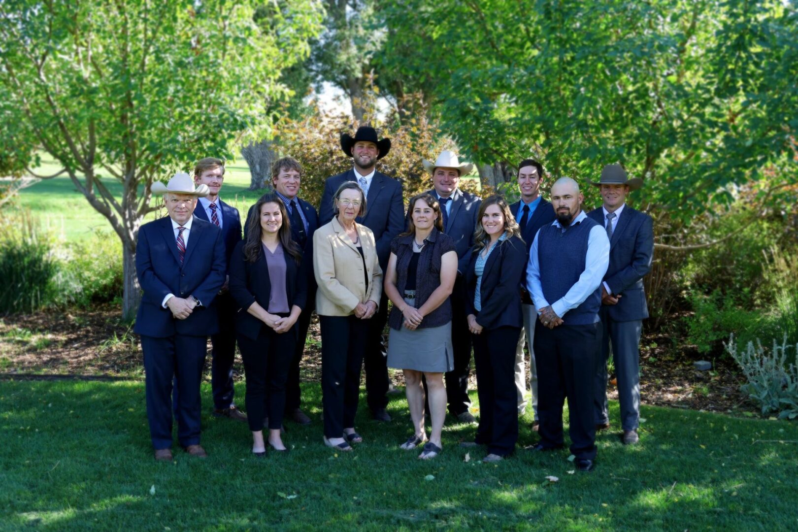 A group of people in suits and hats standing on top of grass.